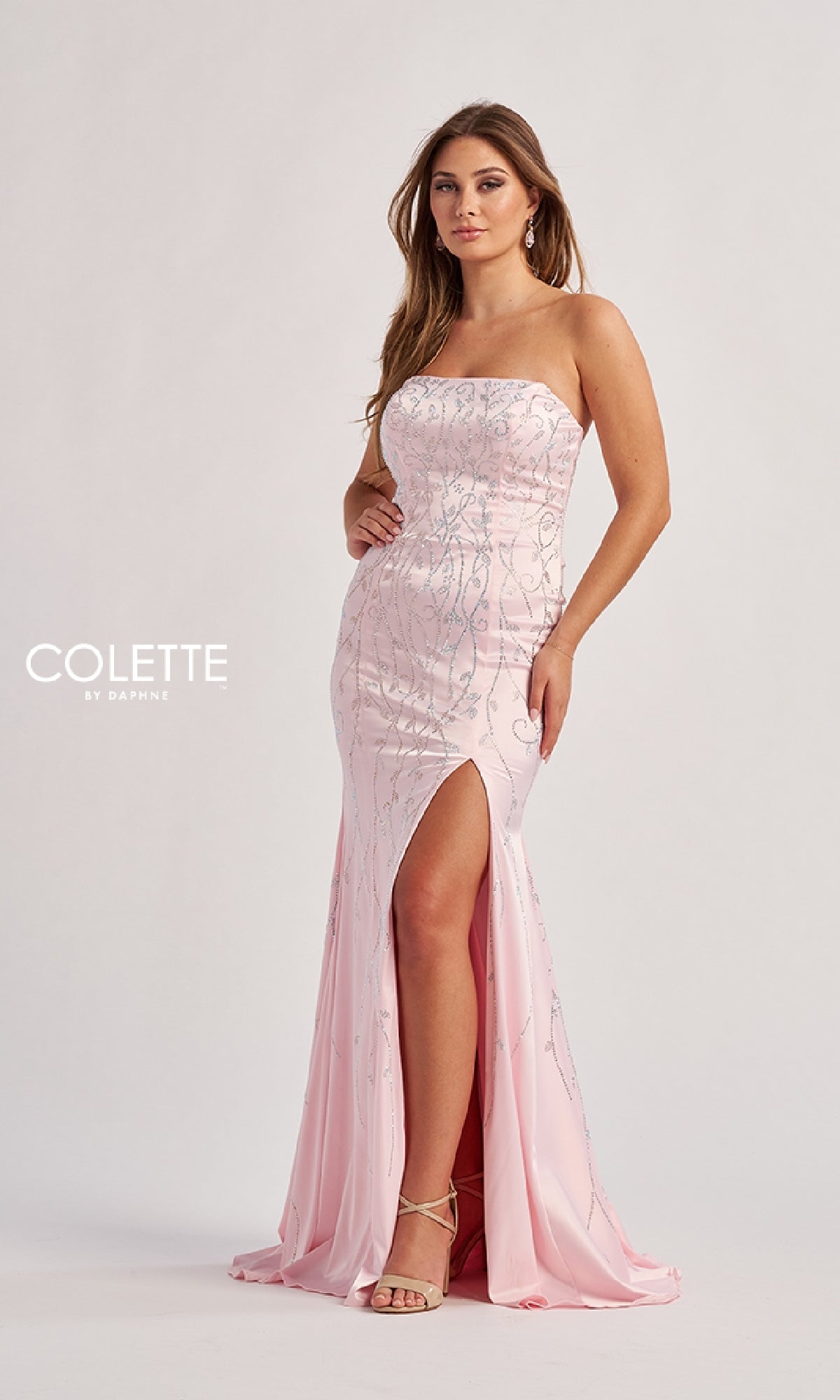 A woman models the Colette CL8570 long prom dress in pink, featuring a strapless neckline, beaded sequin appliques, and a thigh-high slit, paired with strappy heels against a plain background.